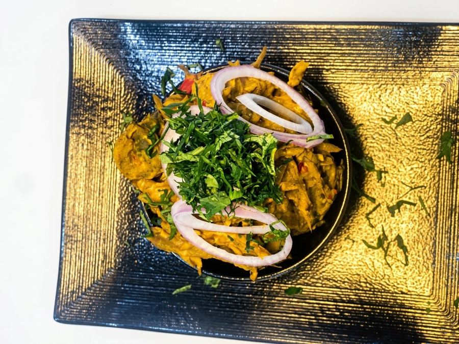 Isiewu in a black bowl on a gold-lit plate, topped with utazi and onion rings