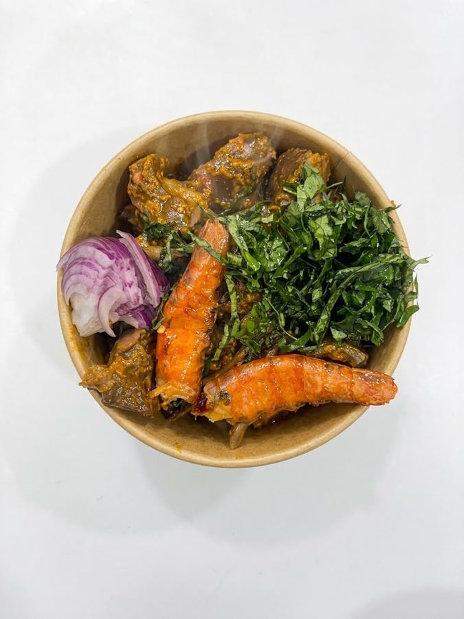 Nkwobi in a kraft bowl with oporo, utazi and red onion