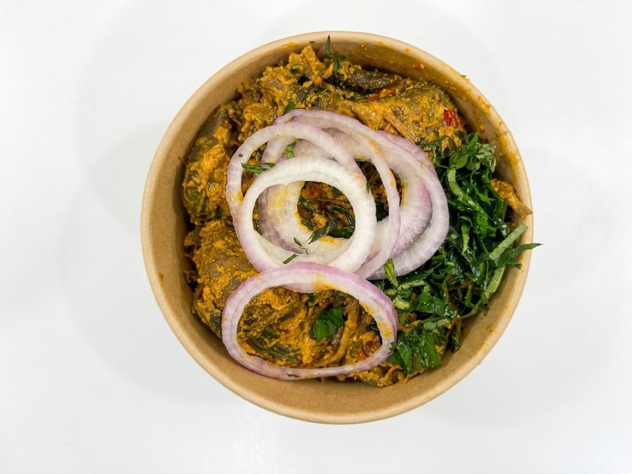 Isiewu in a kraft delivery bowl with onion rings and utazi