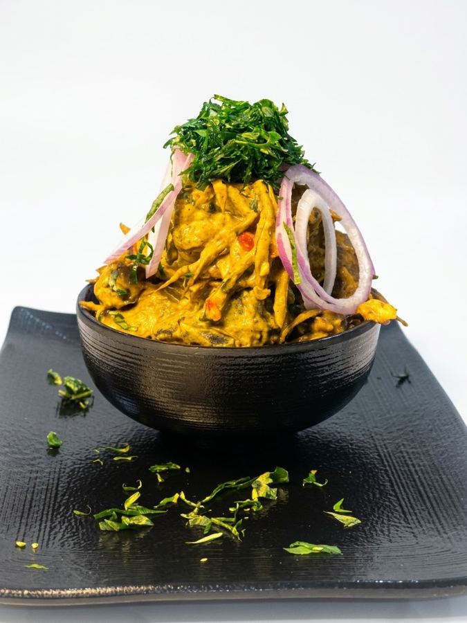 Isiewu piled high in a black bowl, topped with utazi and onion rings
