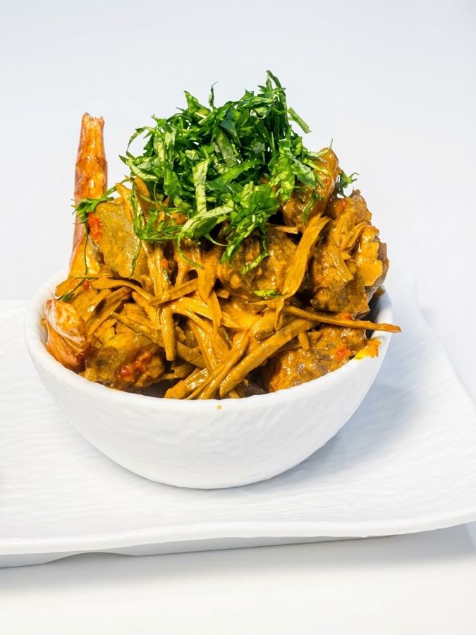 Nkwobi in a white bowl, topped with shredded utazi leaves and oporo